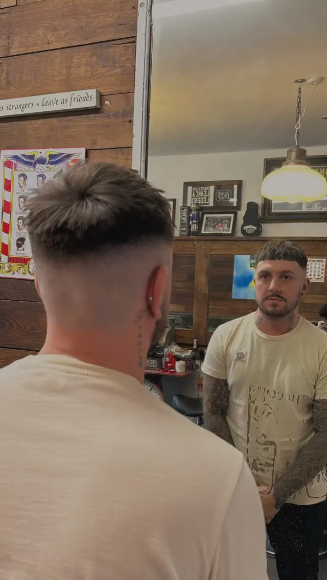 A barber and client mid-conversation at Dapper Chaps, with the shop's wall signage behind them